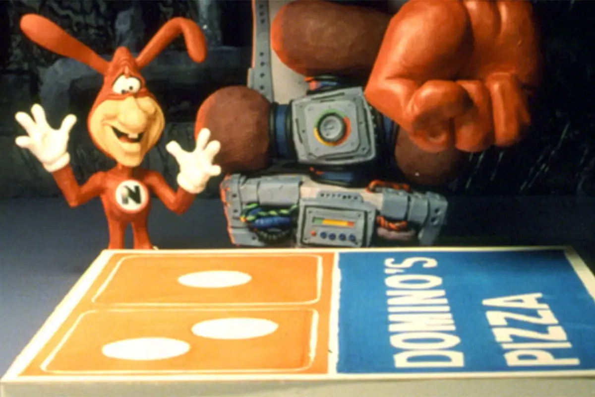 A red rabbit mascot with long ears and a white 'N' on his chest waves enthusiastically while standing behind a Domino's…