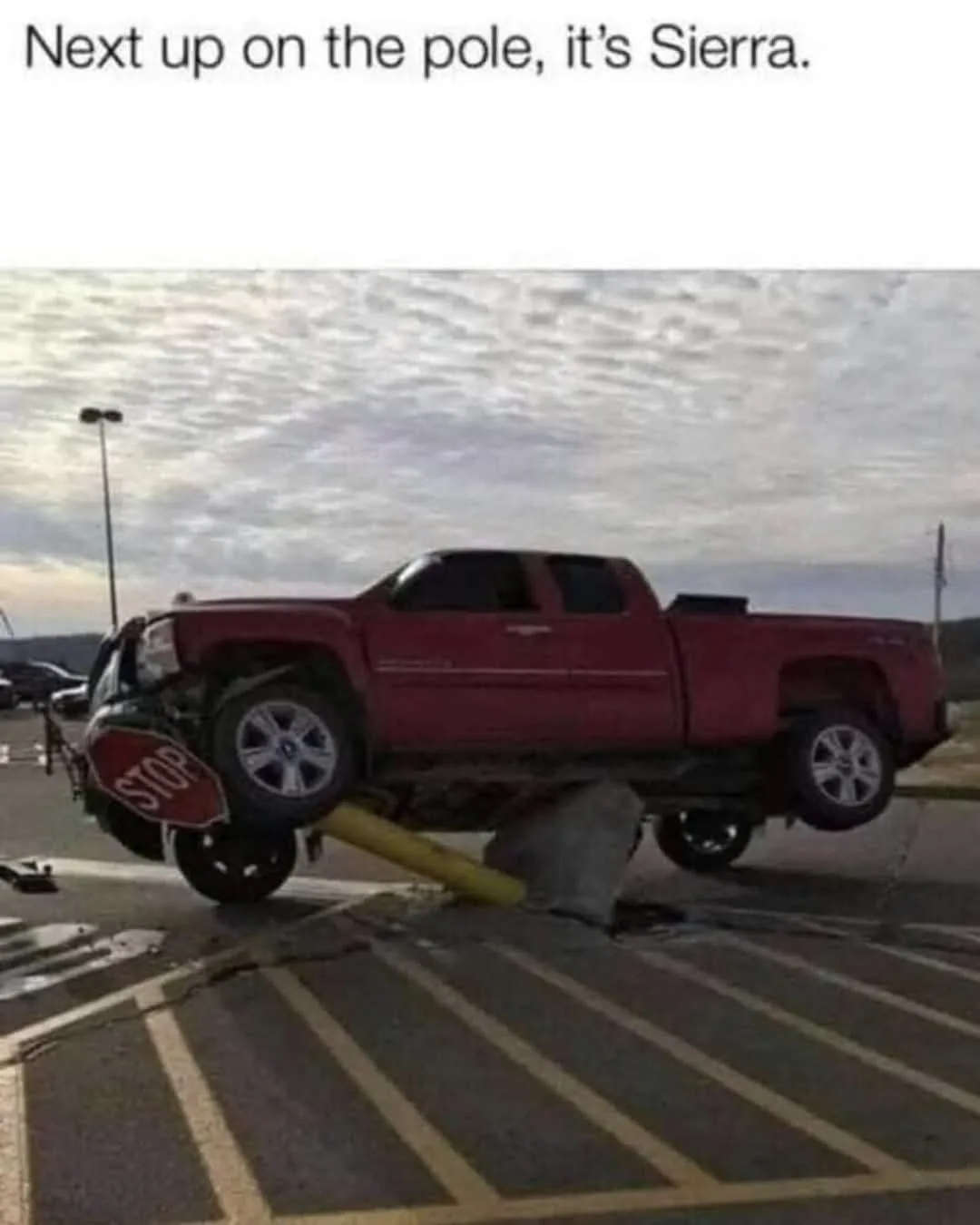 A red pickup truck is visibly stuck with its front end resting on a yellow pole, while its rear end is elevated off the…