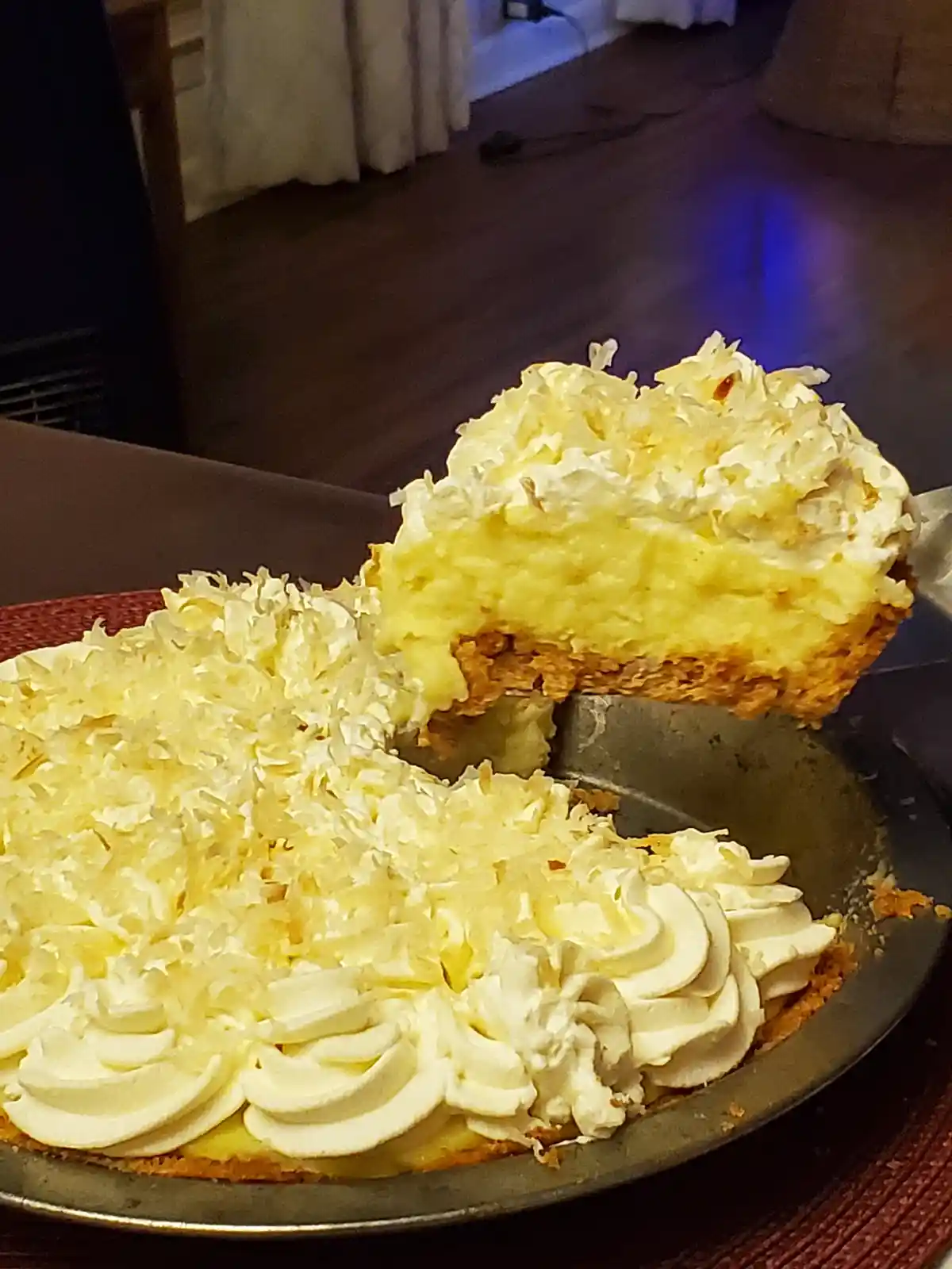 A close-up photo shows a slice of coconut cream pie being lifted from its metal pie dish with a pie server. The pie has a…