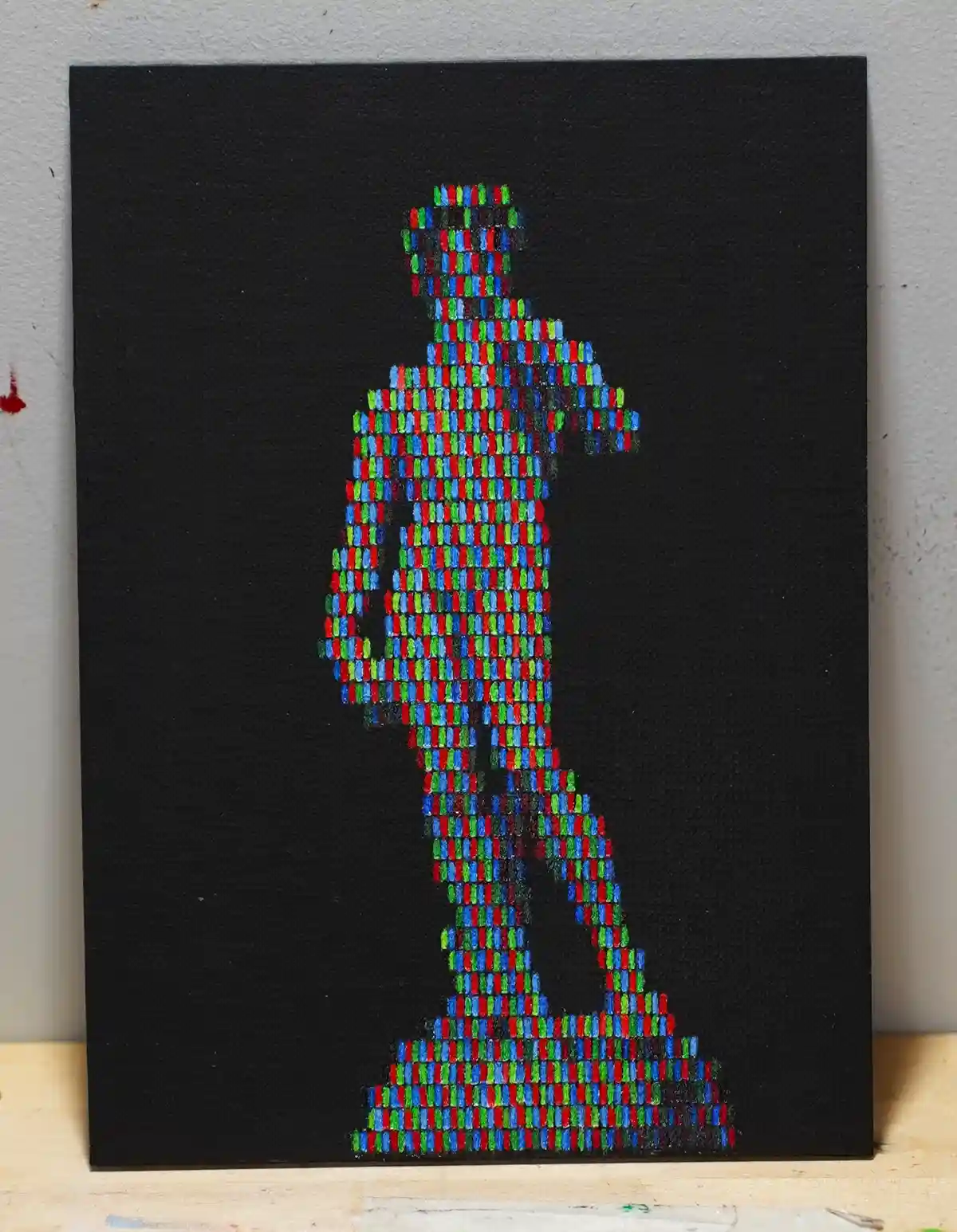 A painting on black canvas depicts a human figure made of colorful vertical pixel-like strokes in red, green, and blue…
