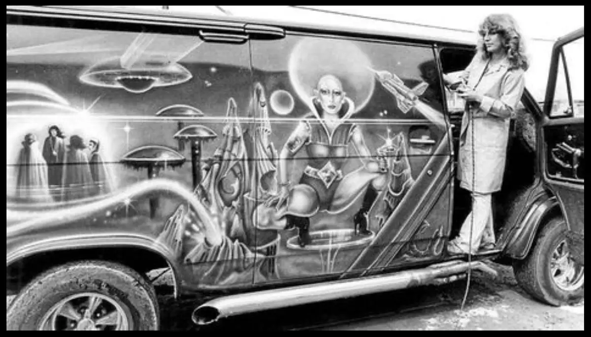 A black-and-white photo shows a woman with long curly hair standing in the open door of a van. The van's side is covered in…