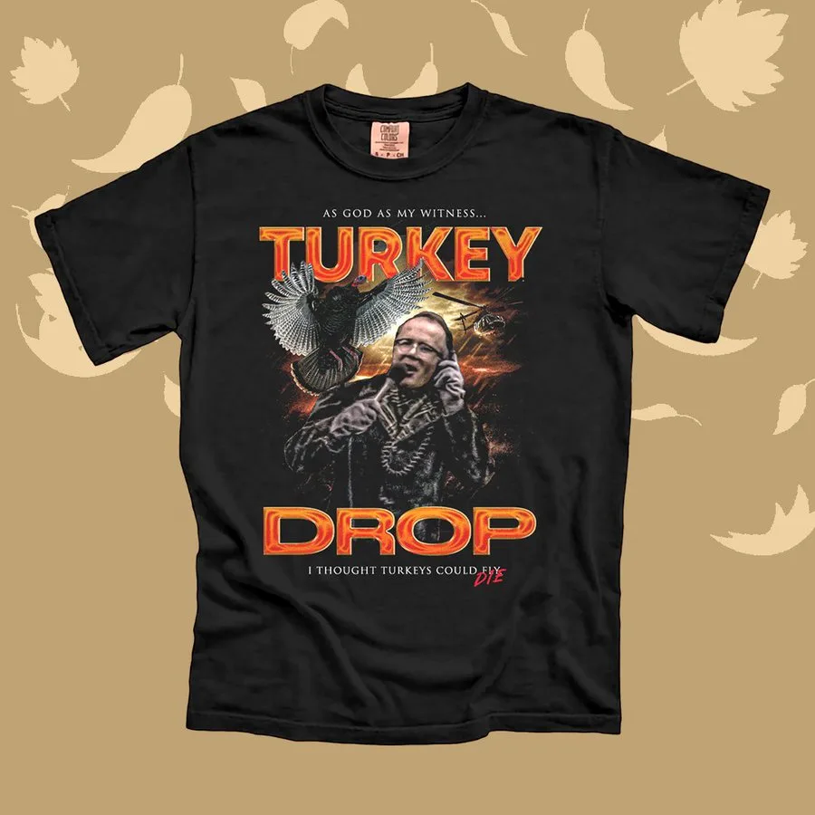 A black t-shirt features a graphic of a man on the phone with a turkey flying behind him, set against a fiery background…