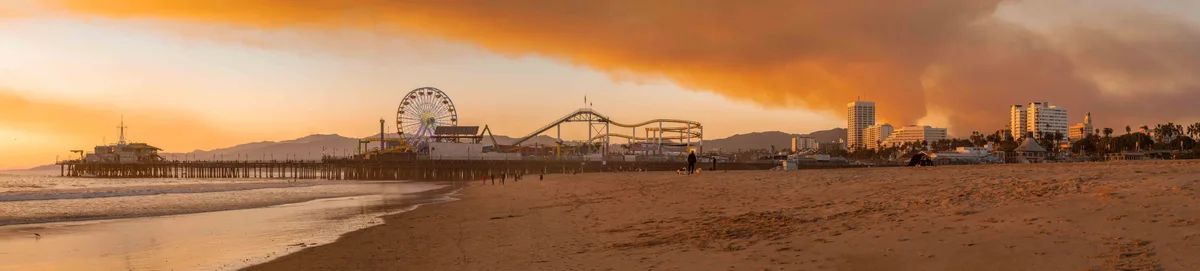 a panoramic photo of the santa monica pier at sunset, showing a ferris wheel, roller coaster, and beach with people, but the…