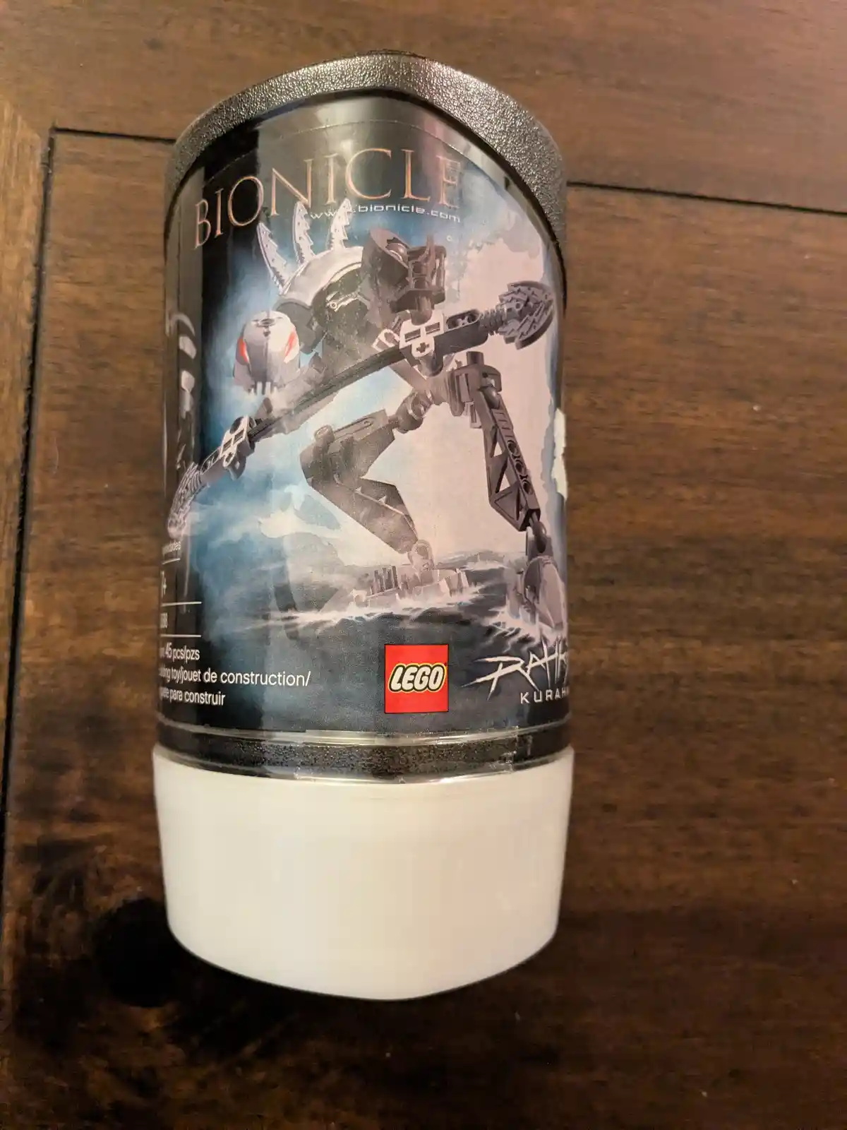 A cylindrical LEGO Bionicle toy package, featuring the character Rahi Kurah, is repurposed as a tumbler or cup, sitting on a…