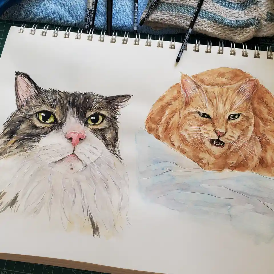 A watercolor sketchbook page shows two detailed cat portraits: one gray-and-white cat with a neutral expression and one…