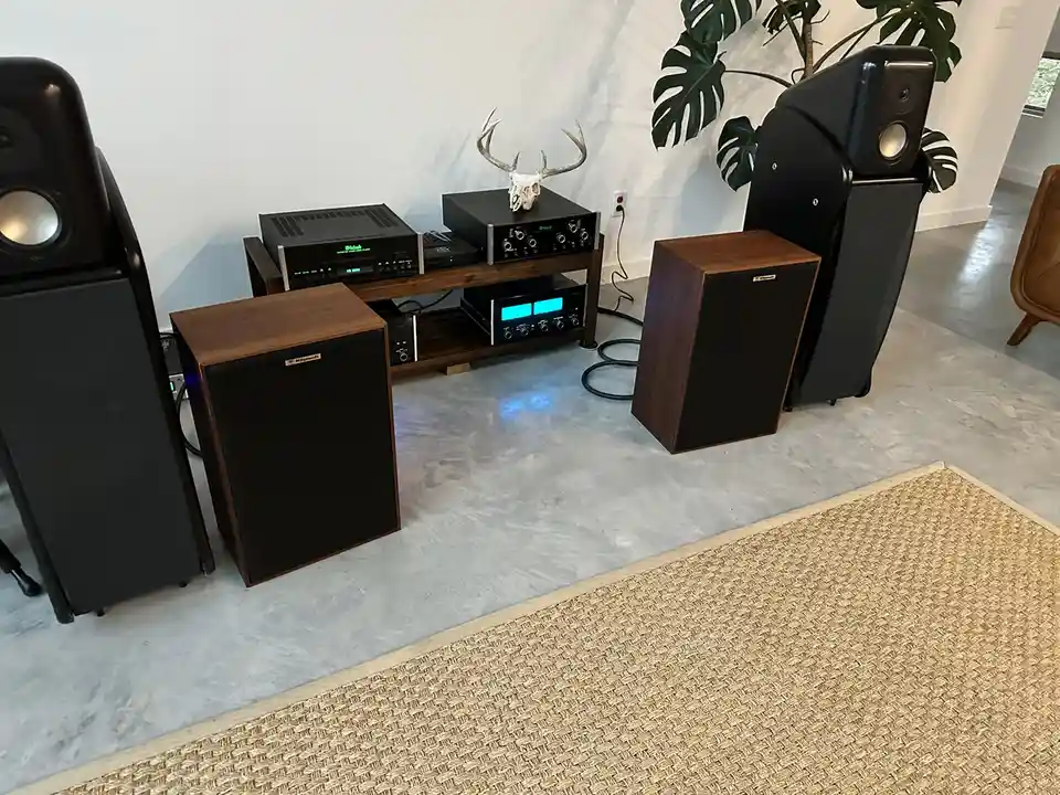 A high-end home audio system with large floor-standing speakers, subwoofers, and electronic components sits on a wooden…