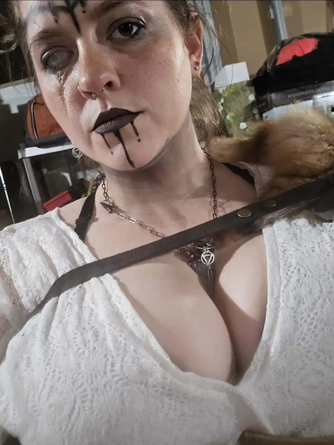 A person with dark makeup, including black streaks dripping from their lips and a black mark on their forehead, looks…