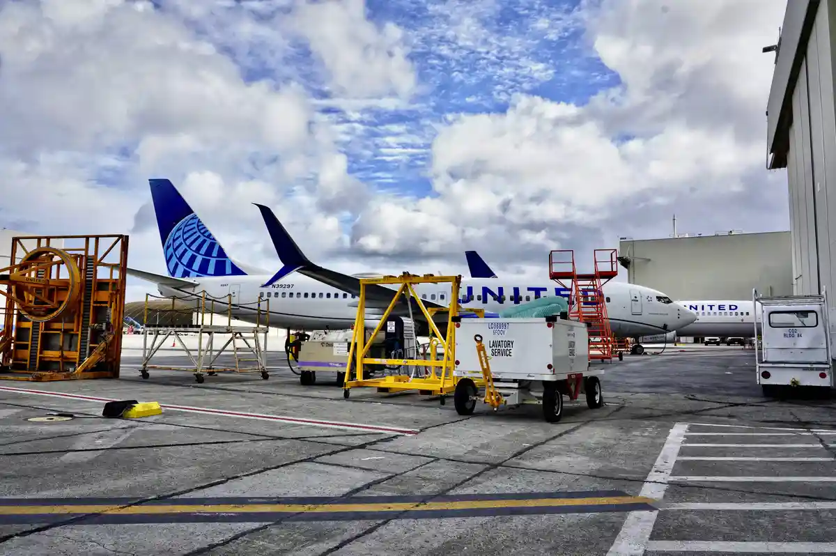 An airport tarmac scene with United Airlines planes parked at gates, surrounded by ground support equipment including a…