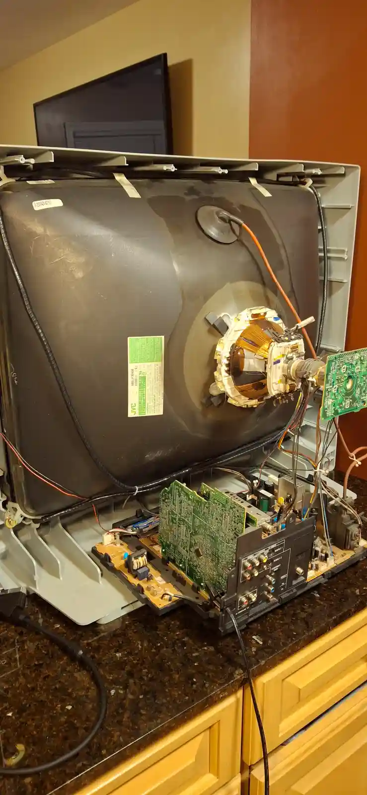 A disassembled JVC CRT television sits on a kitchen counter, its back panel removed to expose internal components like…