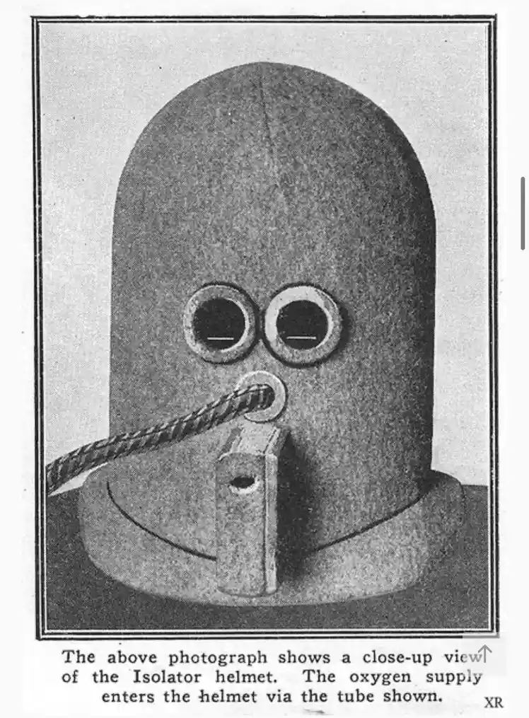 A vintage black-and-white photograph shows a close-up of a bulky, dome-shaped helmet with two circular eye holes and a…