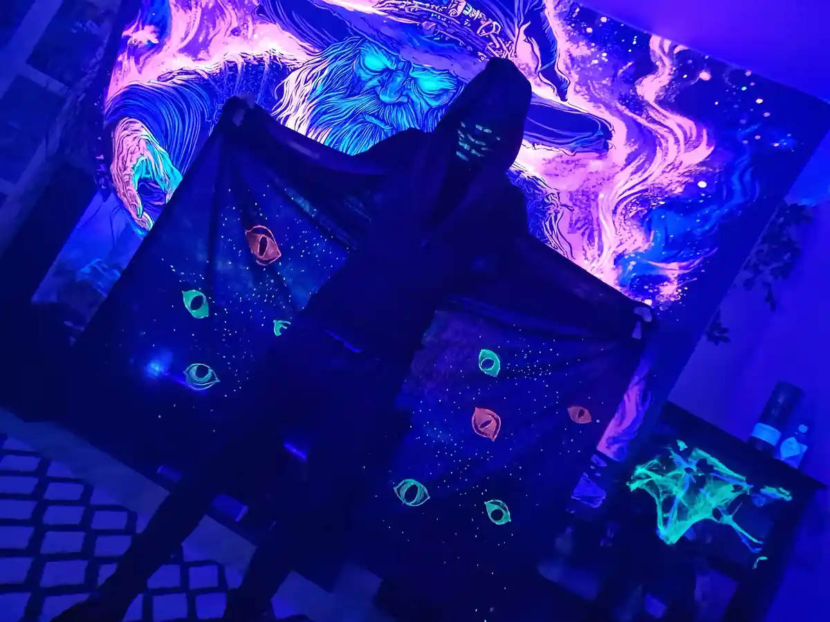 A person in a dark robe with glowing eyes and stars under blacklight, standing in a room with glowing purple and blue walls…