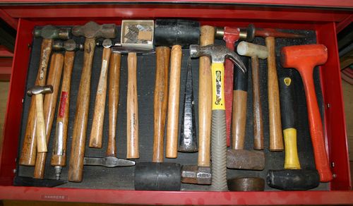 A red toolbox drawer is filled with numerous hammers of various types and sizes, including claw hammers, ball-peen hammers…