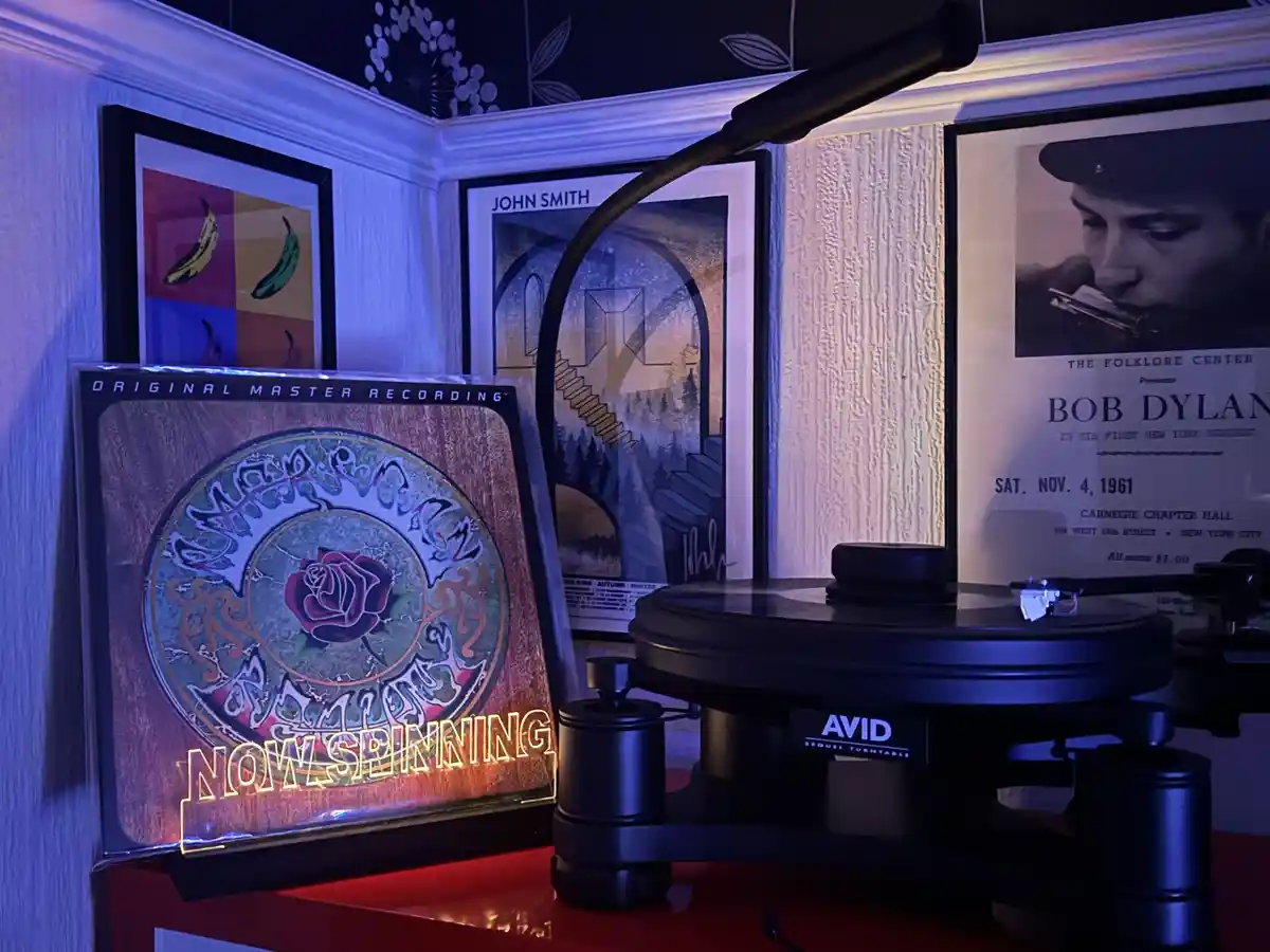 A vinyl record player with a glowing 'NOW SPINNING' sign next to a record sleeve featuring a rose and ornate text. Behind…
