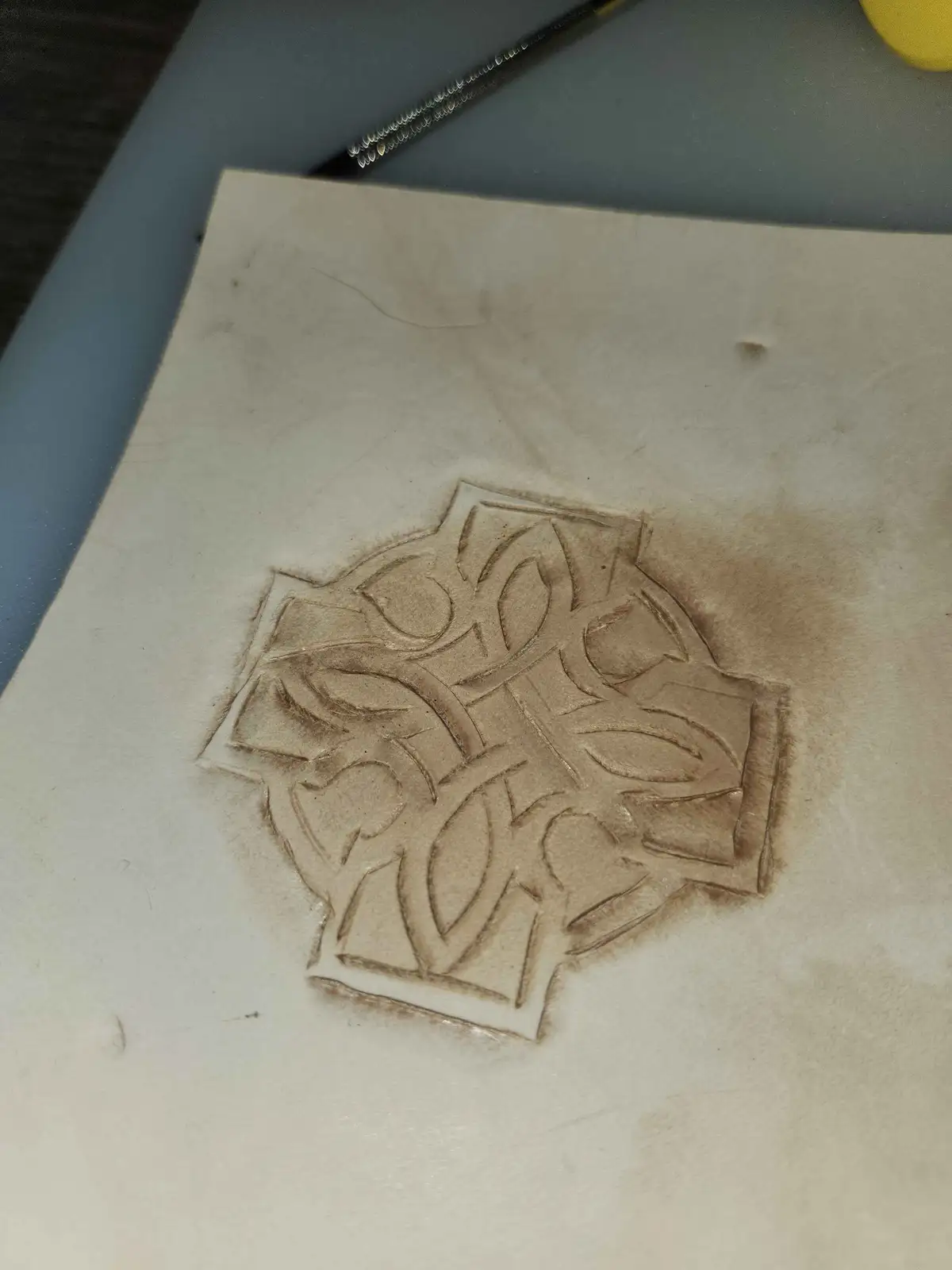 A close-up photo shows a hand-stamped or tooled leather design with intricate, swirling patterns resembling a stylized…