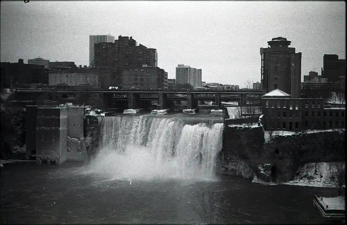 A black-and-white photo of a wide waterfall with a city skyline and bridges in the background, overlaid with the text 'i'm…