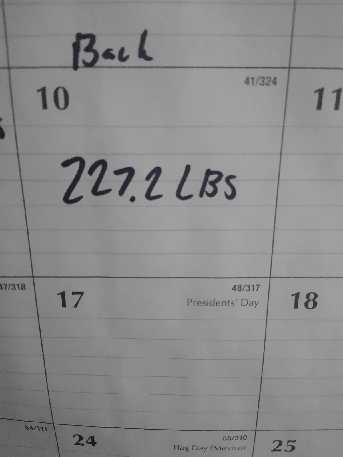 A close-up of a workout log or calendar page showing a handwritten entry for 'Back' on day 10 with the weight '227.2 LBS'…