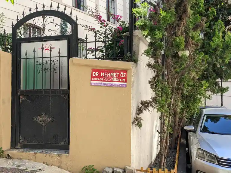 A photo of a black wrought iron gate with 'ELEMENT GARDEN' written on it, next to a street sign reading 'DR. MEHMET ÖZ…