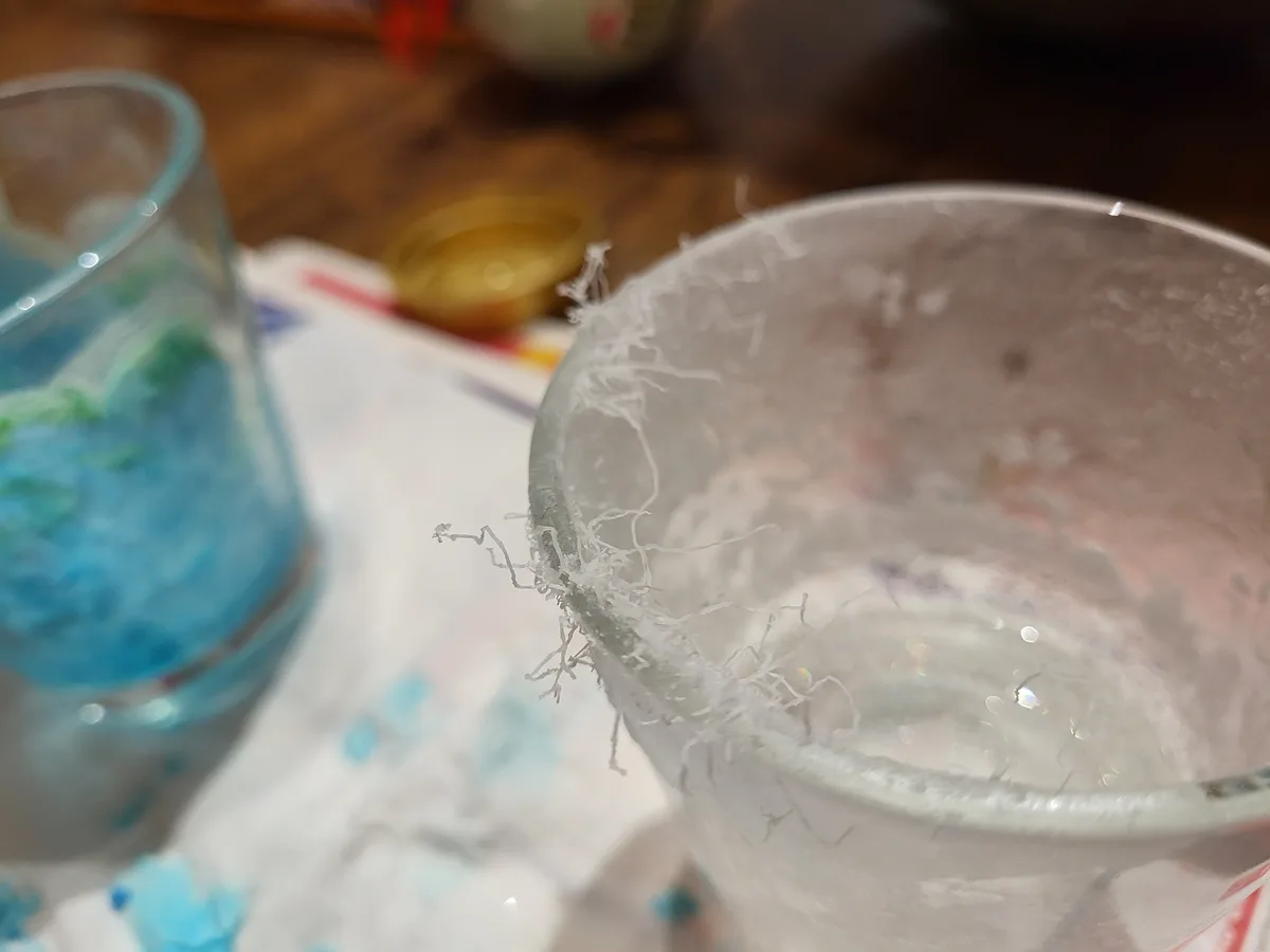 A close-up photo shows the rim of a glass heavily coated in white, stringy, crystalline residue, resembling frost or salt…