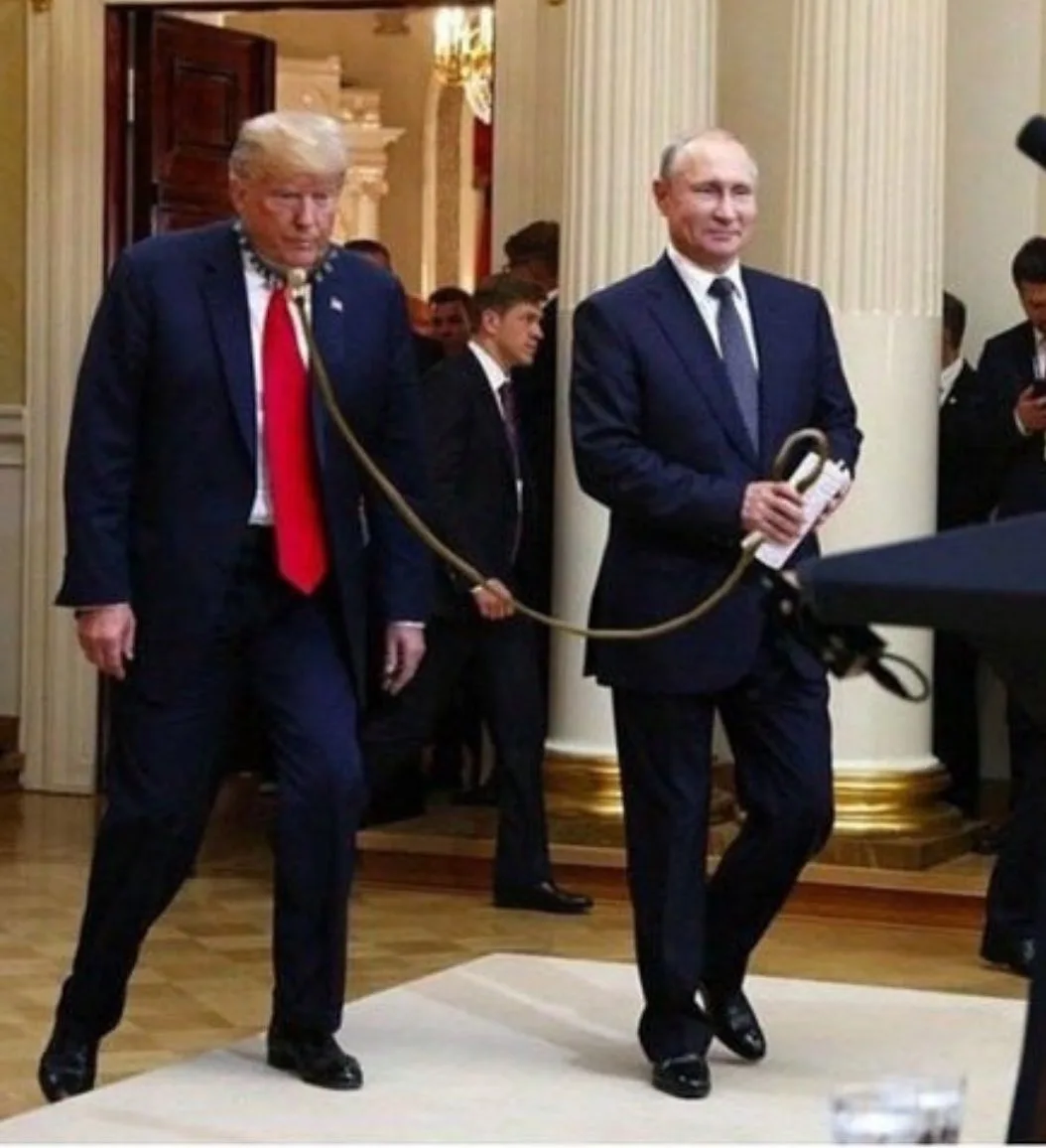 Two men in suits walk side-by-side in an ornate hallway; one man holds a leash attached to the other man's neck, who is…