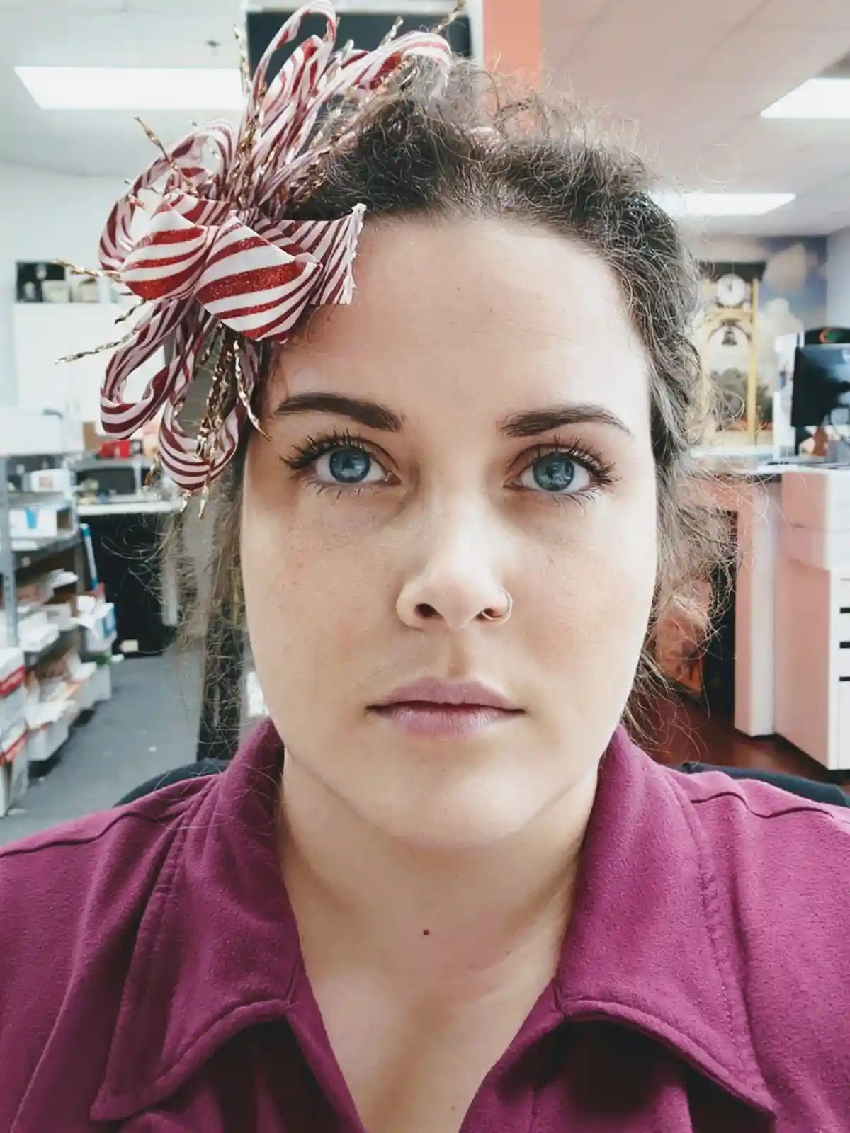 A woman with blue eyes and a nose ring stares directly at the camera with a deadpan expression while wearing a large…