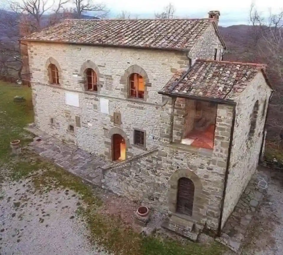 an aerial photo of a rustic stone building with a tiled roof, set in a rural landscape with bare trees and hills in the…