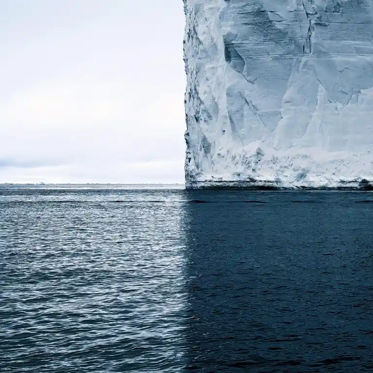 A towering, sheer iceberg stands in calm, dark blue water under an overcast sky. The image is overlaid with the text 'i'm…
