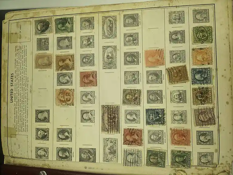 An old, yellowed stamp album page displaying numerous vintage U.S. postage stamps from 1847-1911, arranged in columns with…