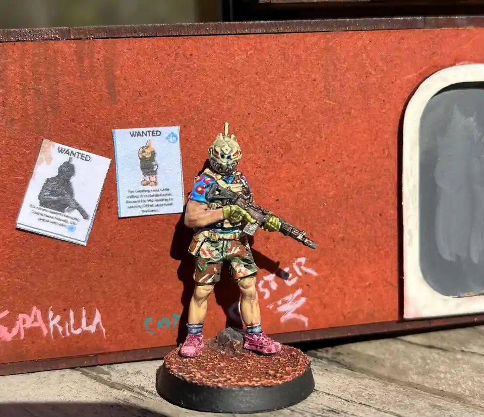 A painted miniature figure of a soldier with a colorful, patterned outfit and pink shoes stands on a rocky base in front of…