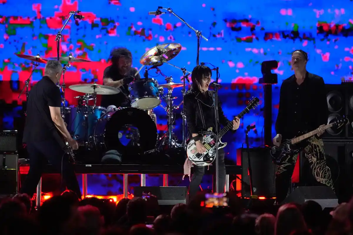 A live band performance photo shows four musicians on stage with a drummer, two guitarists, and a bassist. The bassist on…