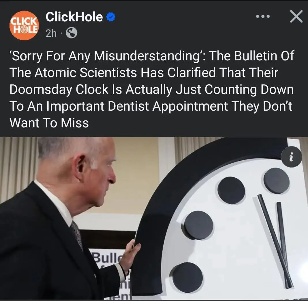 A man in a suit stands beside a large, minimalist Doomsday Clock with black hands and dots on a white face. The overlaid…