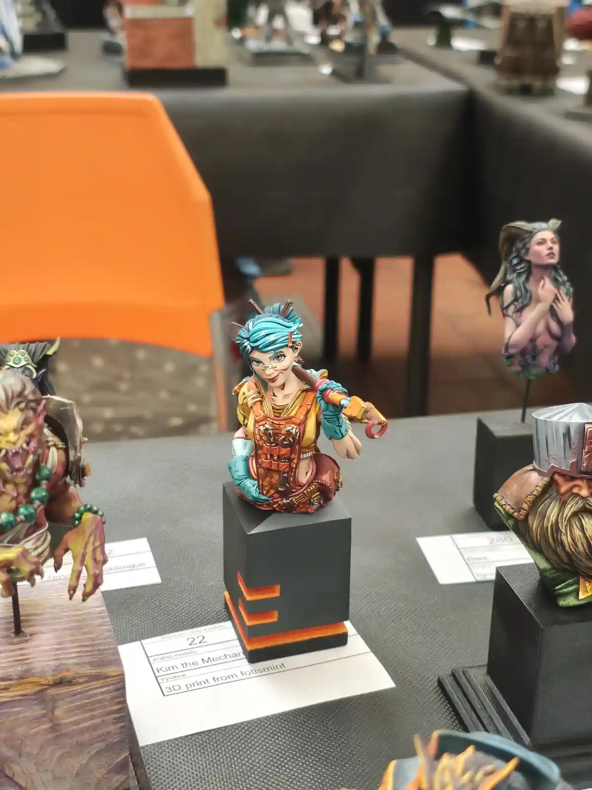 A painted miniature figurine of a female character with blue hair and mechanical gear, labeled 'Kim the Mechanic' on a…