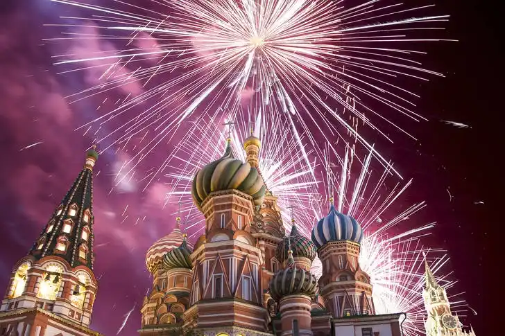 A vibrant nighttime photo of St. Basil's Cathedral in Moscow, Russia, with dazzling white fireworks exploding above its…