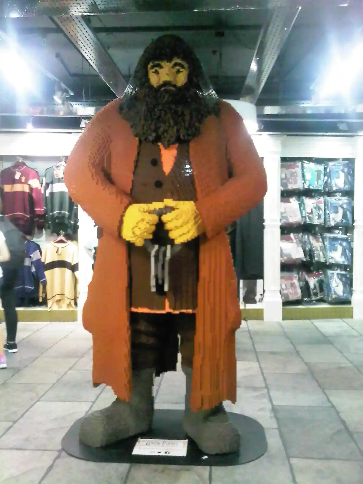 A large, life-sized statue of the character Hagrid from Harry Potter, constructed entirely from LEGO bricks, stands on a…