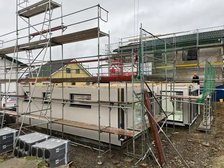 A construction site shows a modern house under scaffolding with workers and building materials, overlaid with the text 'i'm…