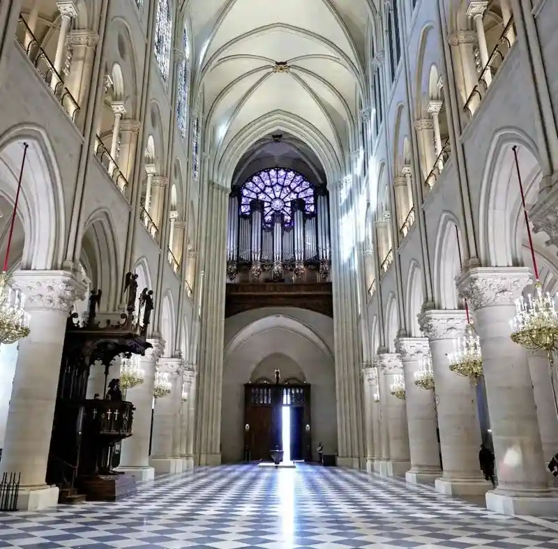 A wide-angle shot of the interior of a grand cathedral with high vaulted ceilings, stone columns, and a checkered floor. A…