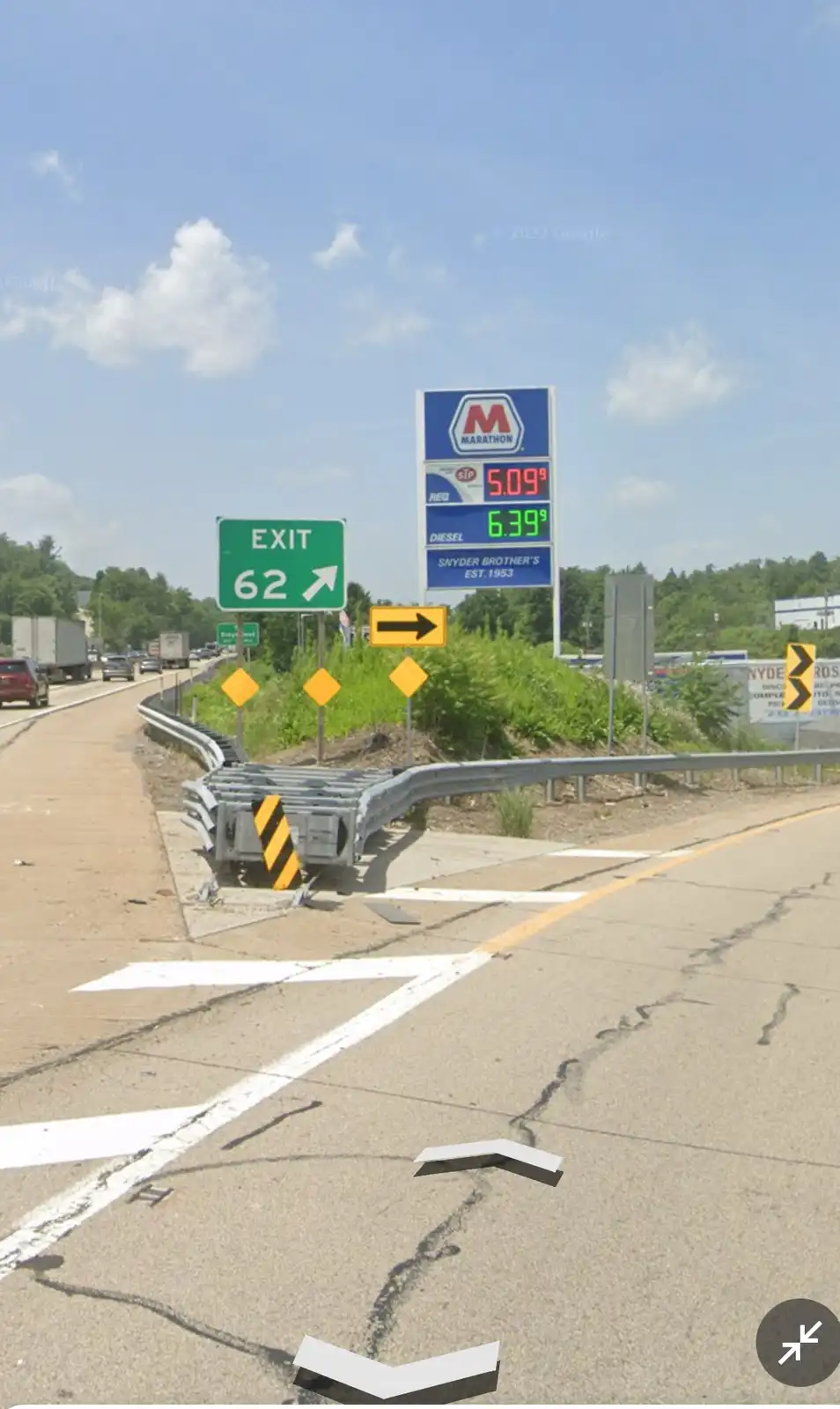 A highway scene with a green 'EXIT 62' sign and a Marathon gas station sign showing prices of $5.09 and $6.39. The image has…