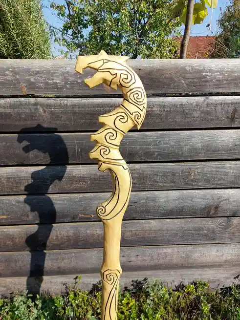 A hand-carved wooden staff with a dragon head at the top, featuring intricate spiral patterns, leans against a weathered…