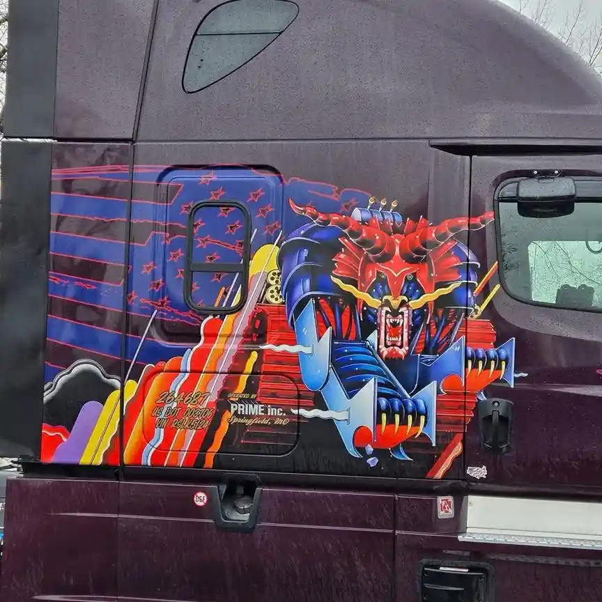 A close-up of a purple semi-truck's side featuring a vibrant, stylized mural of a red and blue demonic creature with horns…