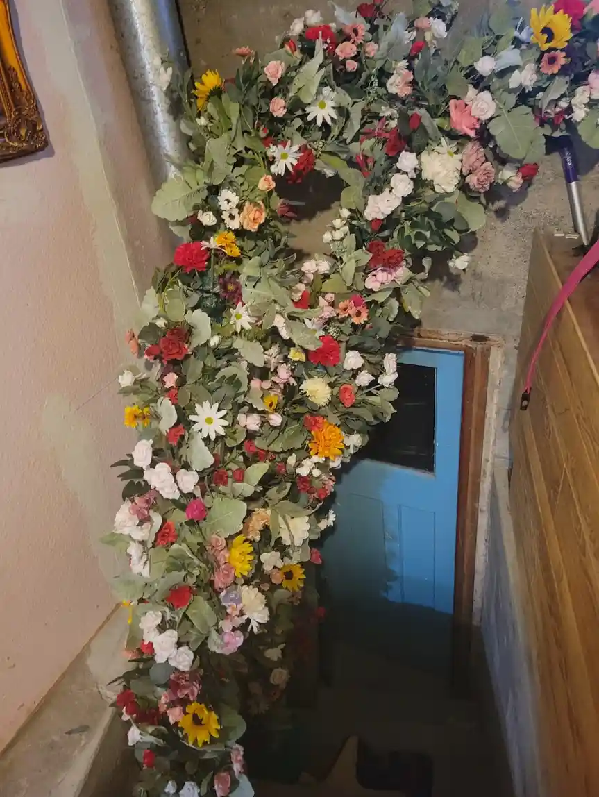 A large, colorful floral arrangement, resembling a wreath or garland made of artificial flowers and greenery, is draped over…