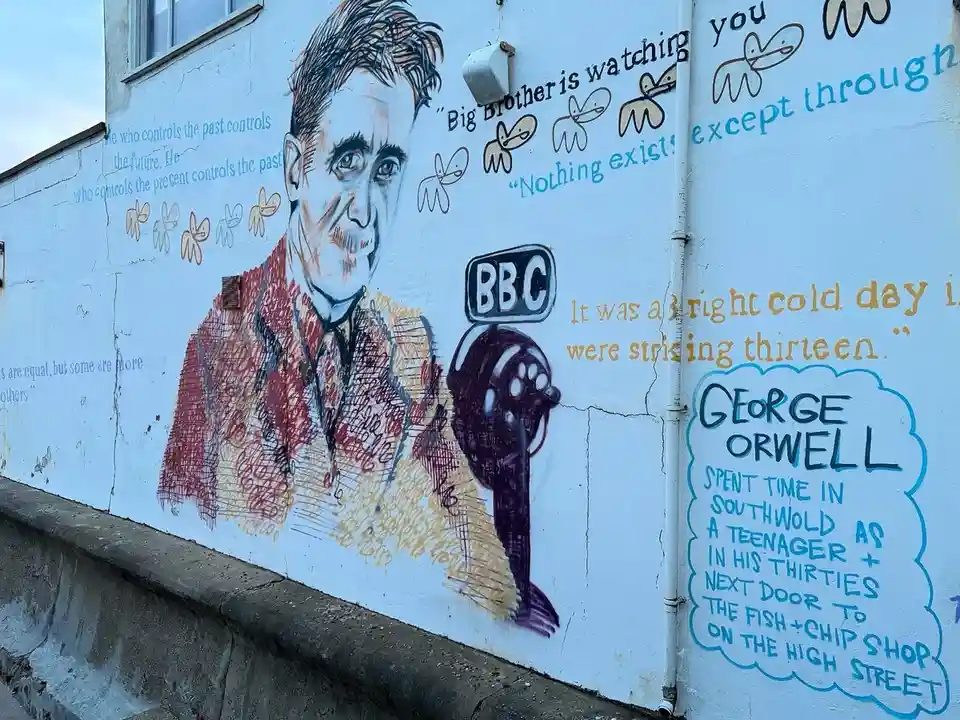 A mural depicts George Orwell holding a microphone with a BBC logo, surrounded by quotes from his novel '1984' like 'Big…