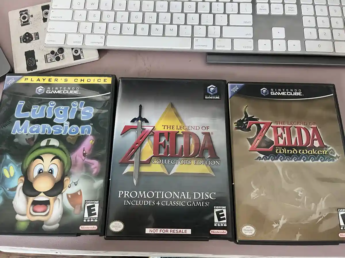 Three Nintendo GameCube game cases are lined up on a desk: Luigi's Mansion, The Legend of Zelda Collector's Edition…