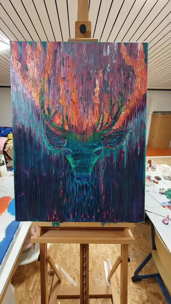 A vibrant, abstract painting of a deer's head on an easel in an art studio, featuring bold strokes of teal, orange, and…