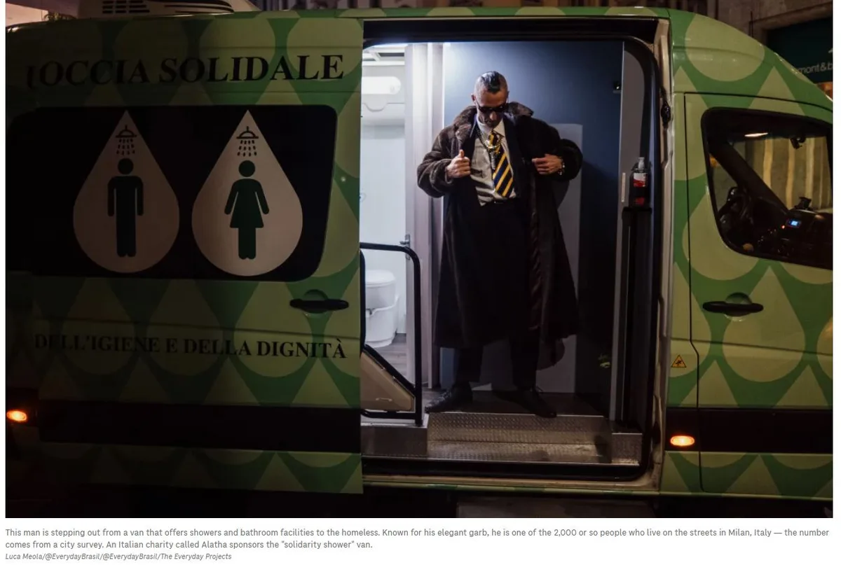 A man in a long dark coat, striped shirt, and yellow-striped tie steps out of a green van with shower and bathroom icons…
