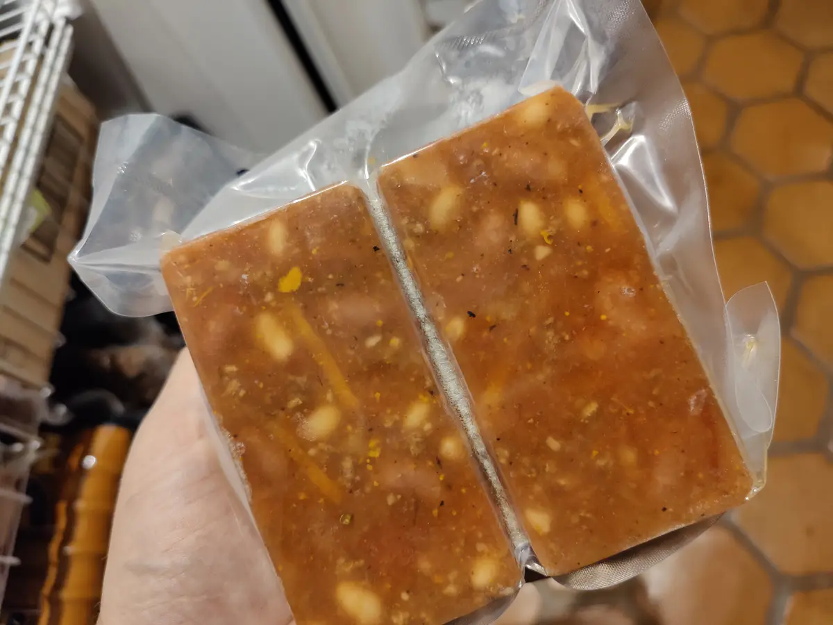 A hand holds a vacuum-sealed plastic bag containing two rectangular, translucent brown blocks with visible white and yellow…