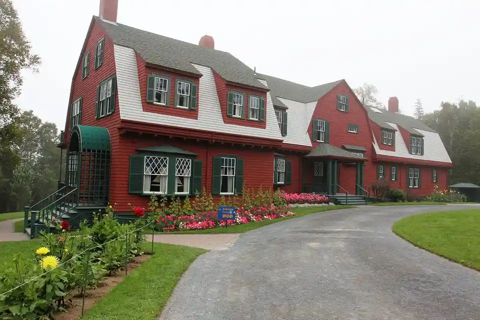 a large red and white colonial-style house with green shutters and a gravel driveway, surrounded by manicured gardens and…