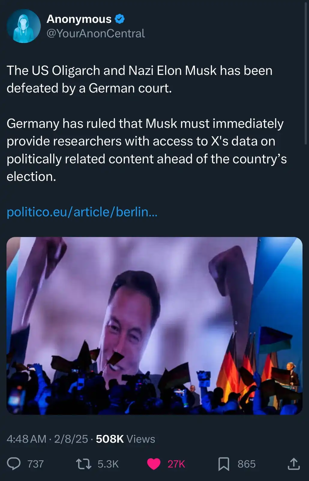 A screenshot of a tweet from 'Anonymous' (@YourAnonCentral) featuring a large image of Elon Musk smiling on a screen above a…