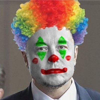 A man in a suit and white face paint with green triangles, red nose, and red lips, wearing a rainbow-colored curly wig. The…