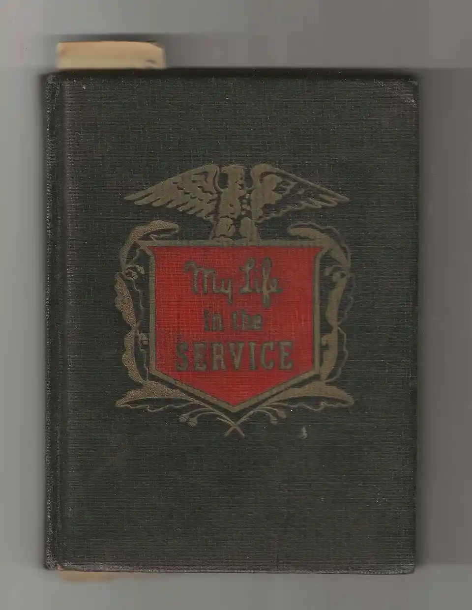 A vintage dark cloth-bound book with a red shield emblem featuring an eagle above it, the text 'My Life in the SERVICE' is…