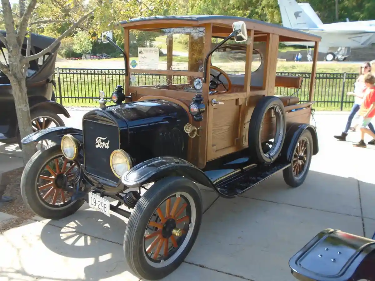 A vintage 1923 Ford Model T with a wooden body and spoked wheels is displayed outdoors, with a sign reading 'HORSELESS…