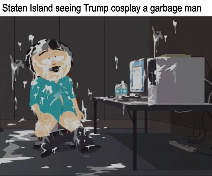 A cartoon character from South Park, covered in white foam, sits on the floor in a messy room with a desk, computer, and…
